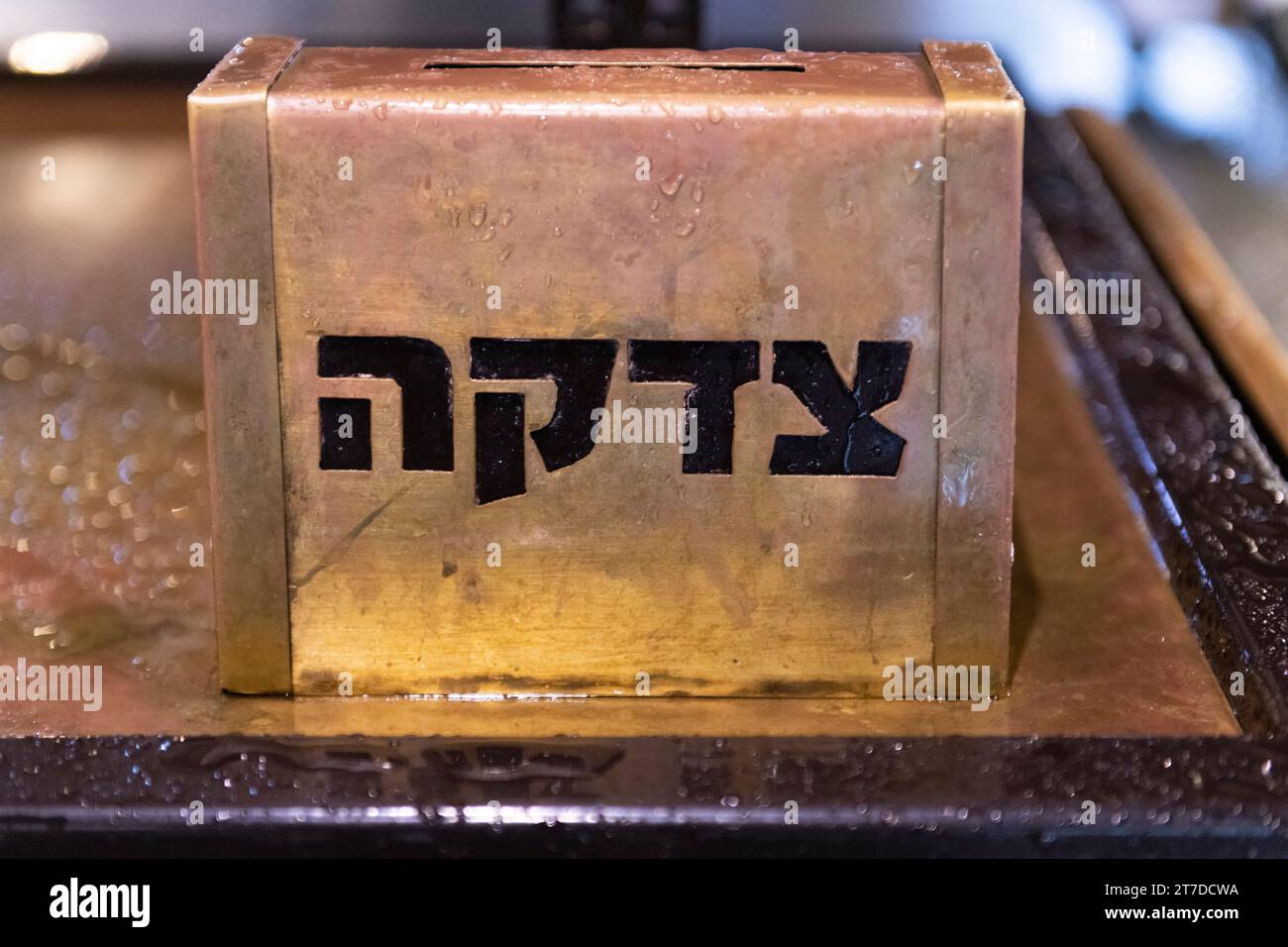 Eine goldene, metallene Tzedakah (ein hebräisches Wort, das „Wohltätigkeit“ bedeutet), die draußen in Jerusalem im Regen auf einem Tisch sitzt. Stockfoto