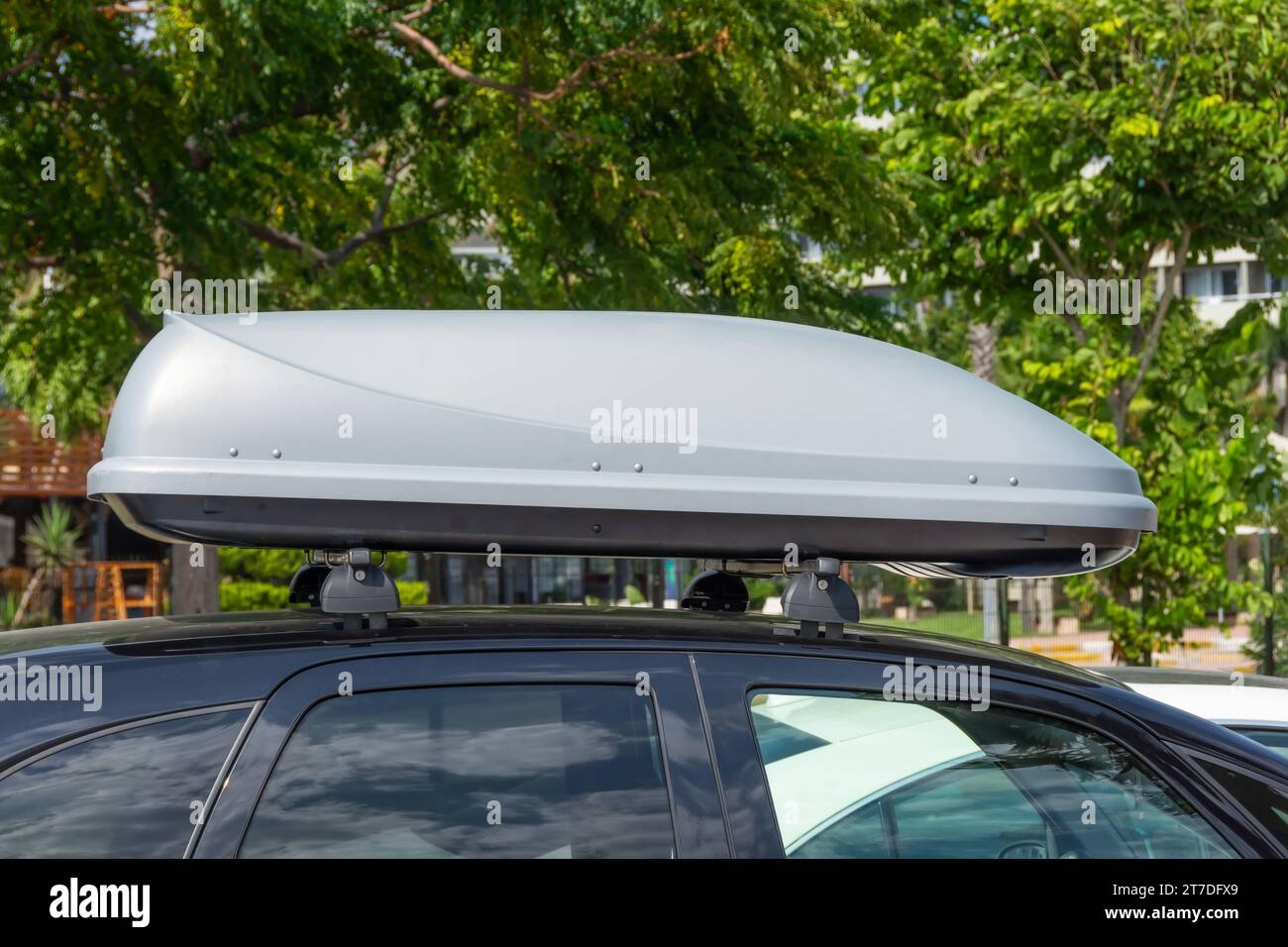 Schwarzer Kunststoff-Cargo auf dem Dach oder Dachträger für unterwegs. Abnehmbarer Aufbewahrungsbehälter, montiert auf dem Dachträger des Autos. Stockfoto