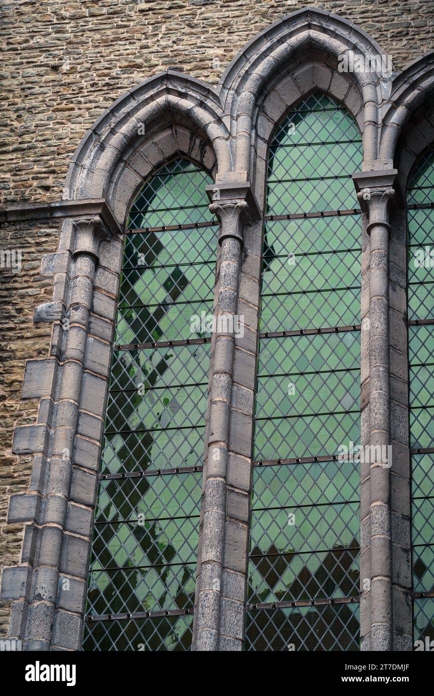 Detail eines großen grünen bogenförmigen Glasfensters einer alten Kirche. Buntglasfenster mit Würfelmotiven. Reflexionen auf dem Fenster. Ziegelwand. Stockfoto