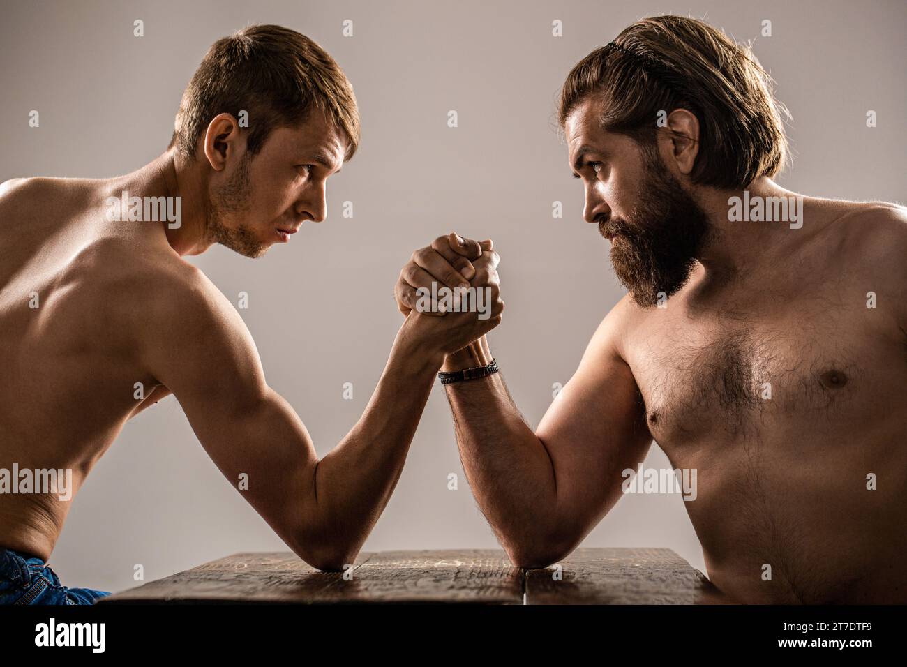 Zwei Mannshände schlossen den Arm, stark und schwach, ungleich. Armringen. Arme mit dünner Hand, großer, starker Arm im Studio Stockfoto