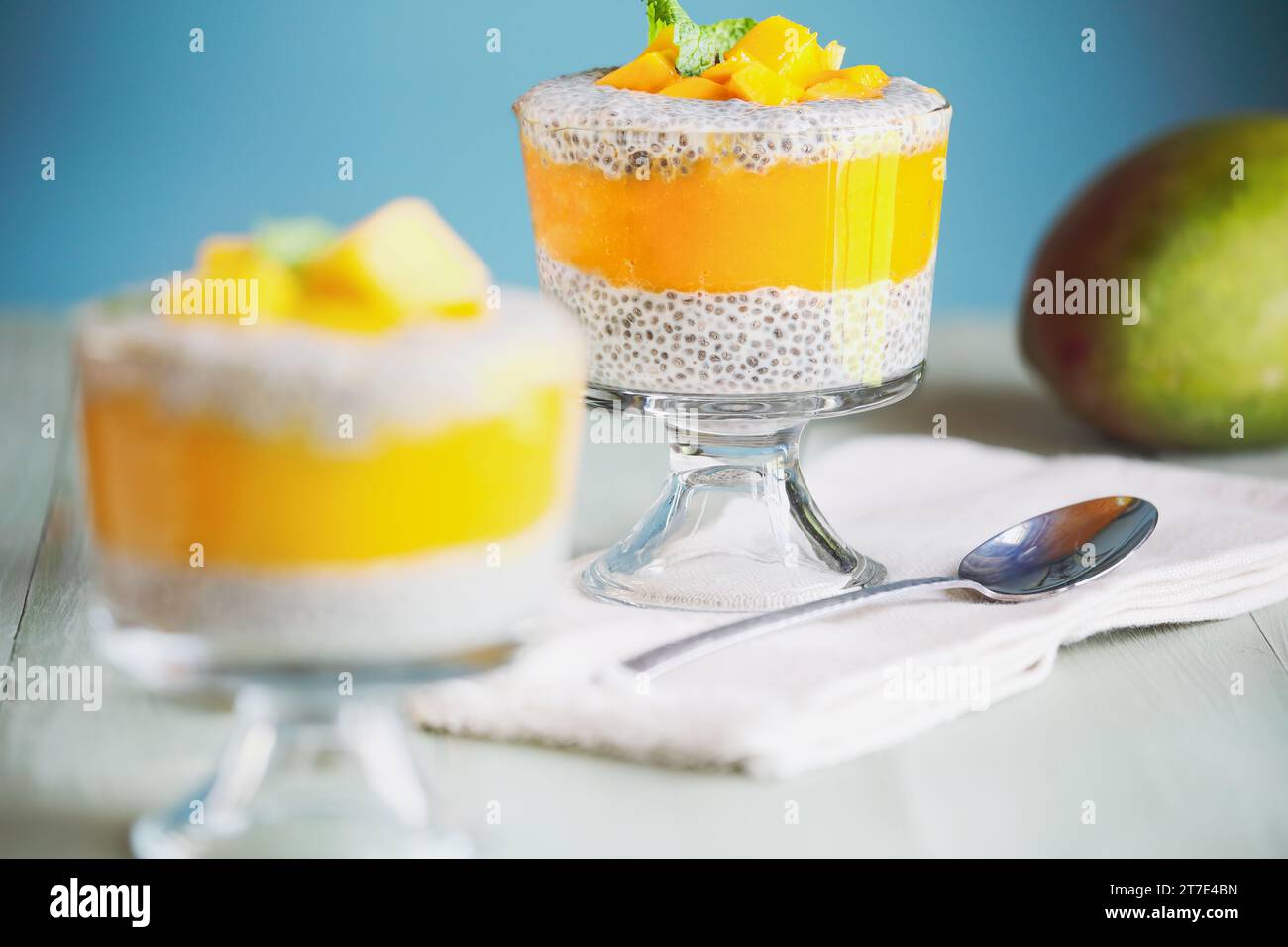 Köstlicher veganer Mango-Chia-Pudding mit frischen Minzquellen in einem Glas auf grünem Holzhintergrund. Selektiver Fokus mit unscharfem Hintergrund. Stockfoto