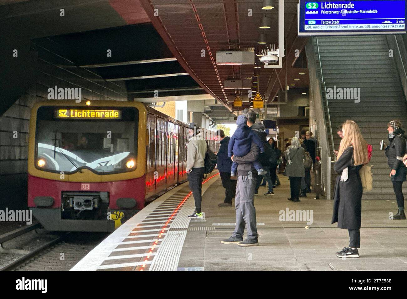 15.11.2023, Berlin, DE - Rot leuchtende Bahnsteigkante am S-Bahnhof Suedkreuz bei Einfahrt eines Zuges. Alltag, Aussen, Aussenaufnahme, Bahn, Bahnhof, Bahnstation, Bahnsteig, Bahnsteigkante, Bahnverkehr, befoerdern, Befoerderung, Berlin, deutsch, Deutschland, einfahren, Einfahrt, Europa, europaeisch, Fahrgaeste, Gesellschaft, Herbst, Jahreszeit, LED-Leitsystem, LED-Leuchten, Leitsystem, leuchtend, Lichtssteuerung, Menschen, Nahverkehr, oeffentlicher Nahverkehr, oeffentlicher Personennahverkehr, OEPNV, Personen, Personenbeförderung, Personentransport, QF, Querformat, rot, S 2, S-Bahn, s-Bahnh Stockfoto