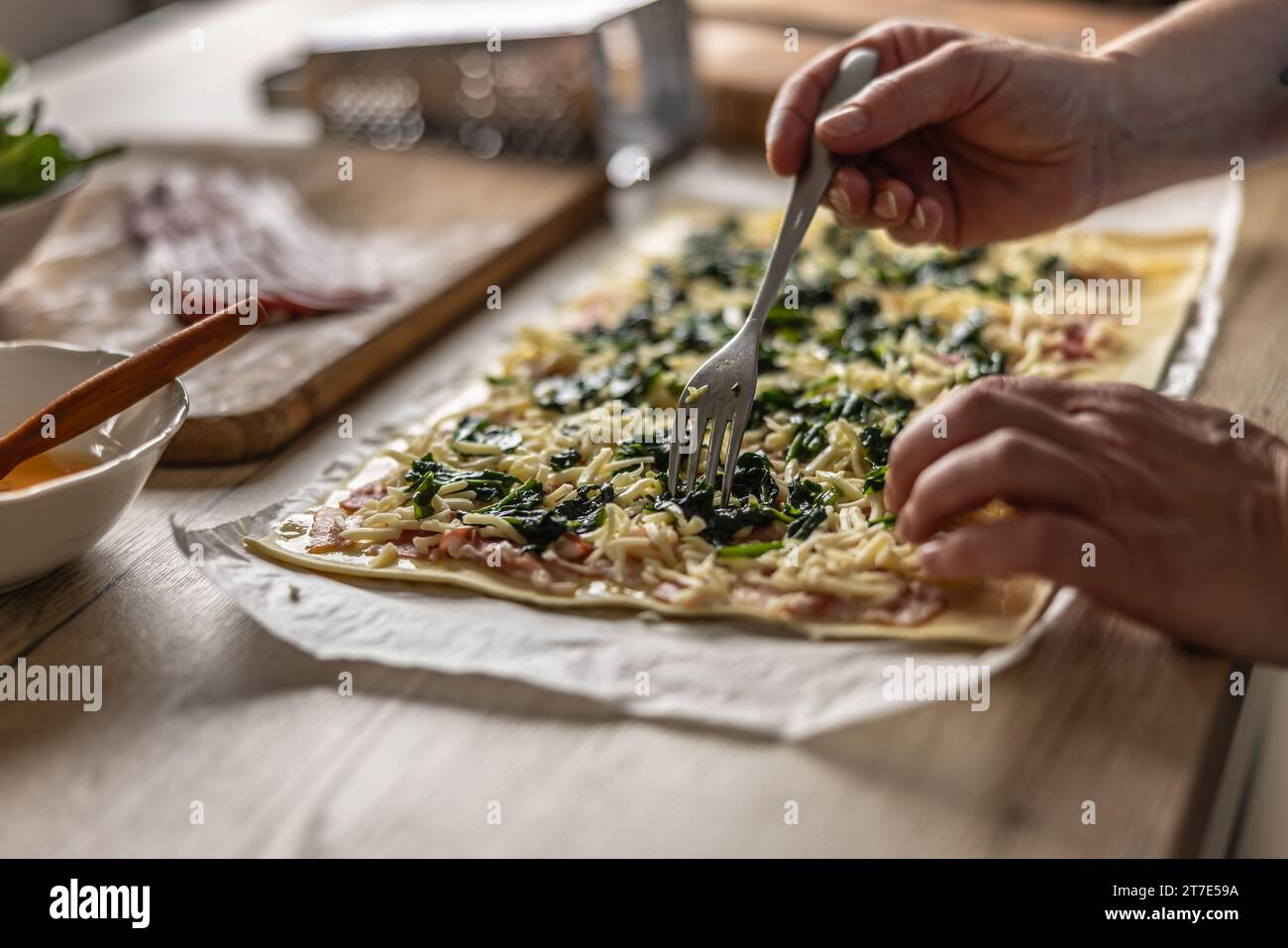 Der Koch bereitet Mini-Pizzakuchen zu, gibt Spinat auf Blätterteig mit Käse und Speck. Rezeptverfahren: 4 von 10 Stockfoto