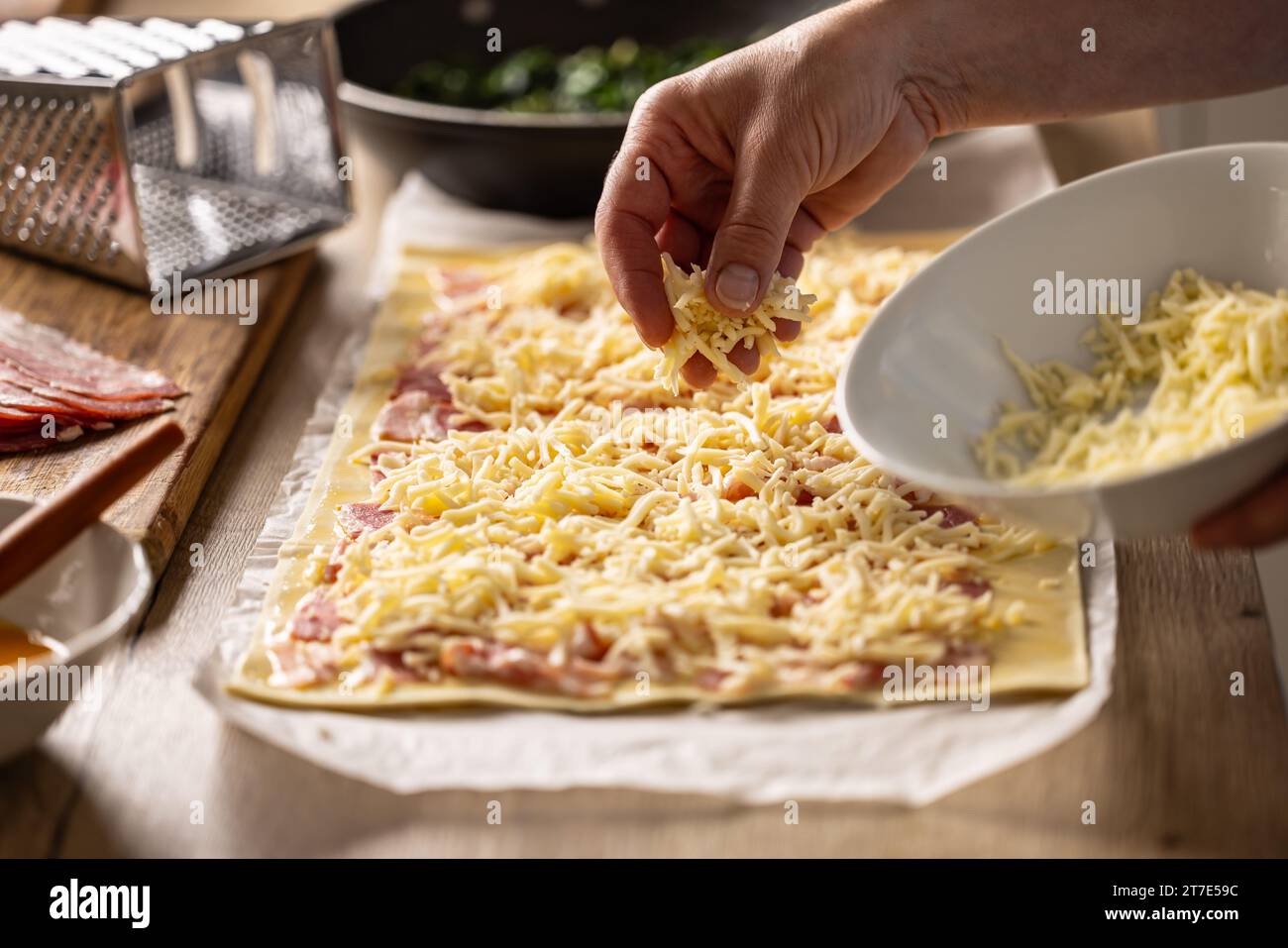 Die weibliche Köchin bereitet Mini-Pizzakuchen zu, streut Käse auf Blätterteig mit Speck. Rezeptverfahren: 3 von 10 Stockfoto