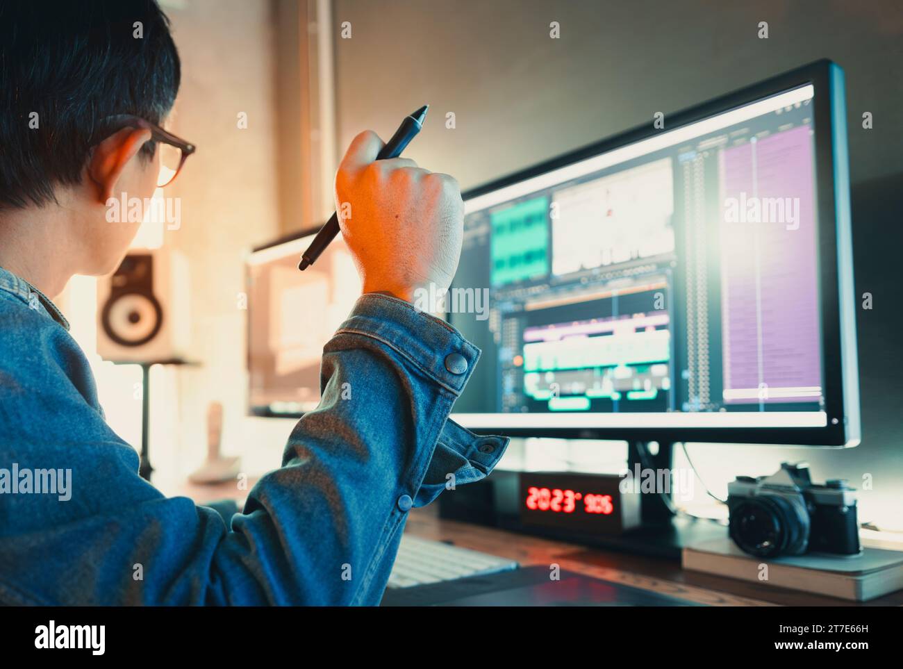 Asiatischer Videoredakteur für männliche Filme in Jeansjacke, arbeitet mit Filmmaterial oder Video in seinem kreativen Bürostudio. Stockfoto