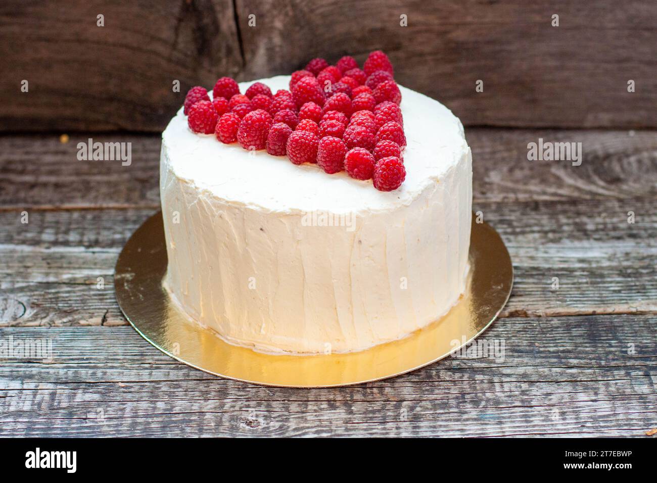 Eleganter weißer Kuchen mit Himbeerherz für St. Valentinstag, Muttertag oder Geburtstag, dekoriert mit frischem Beerenzucker auf hölzernem Hintergrund Stockfoto