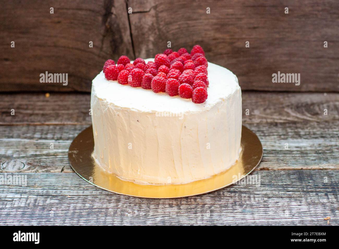 Eleganter weißer Kuchen mit Himbeerherz für St. Valentinstag, Muttertag oder Geburtstag, dekoriert mit frischem Beerenzucker auf hölzernem Hintergrund Stockfoto