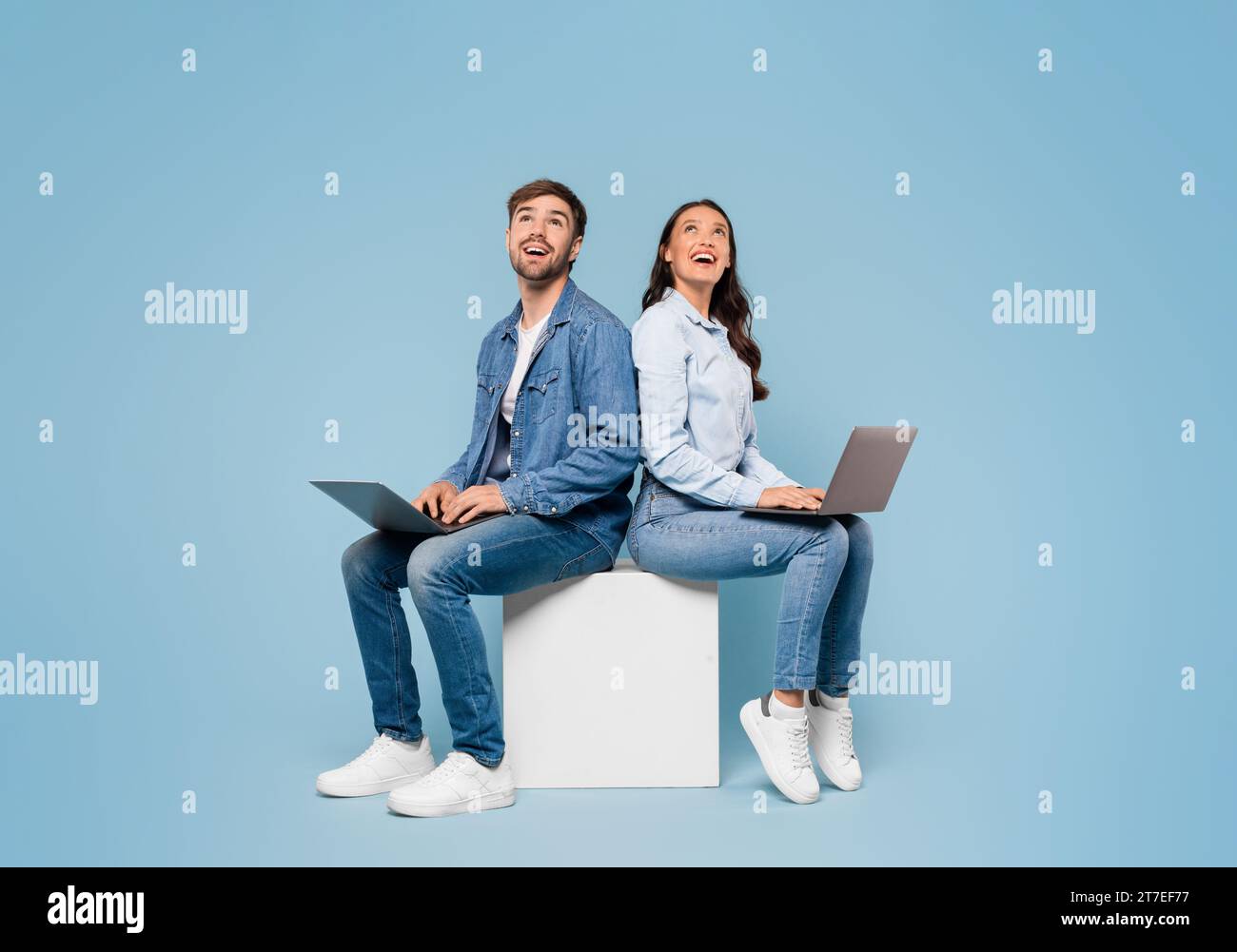 Ein Paar mit Laptops sieht freien Platz auf blauem Hintergrund Stockfoto