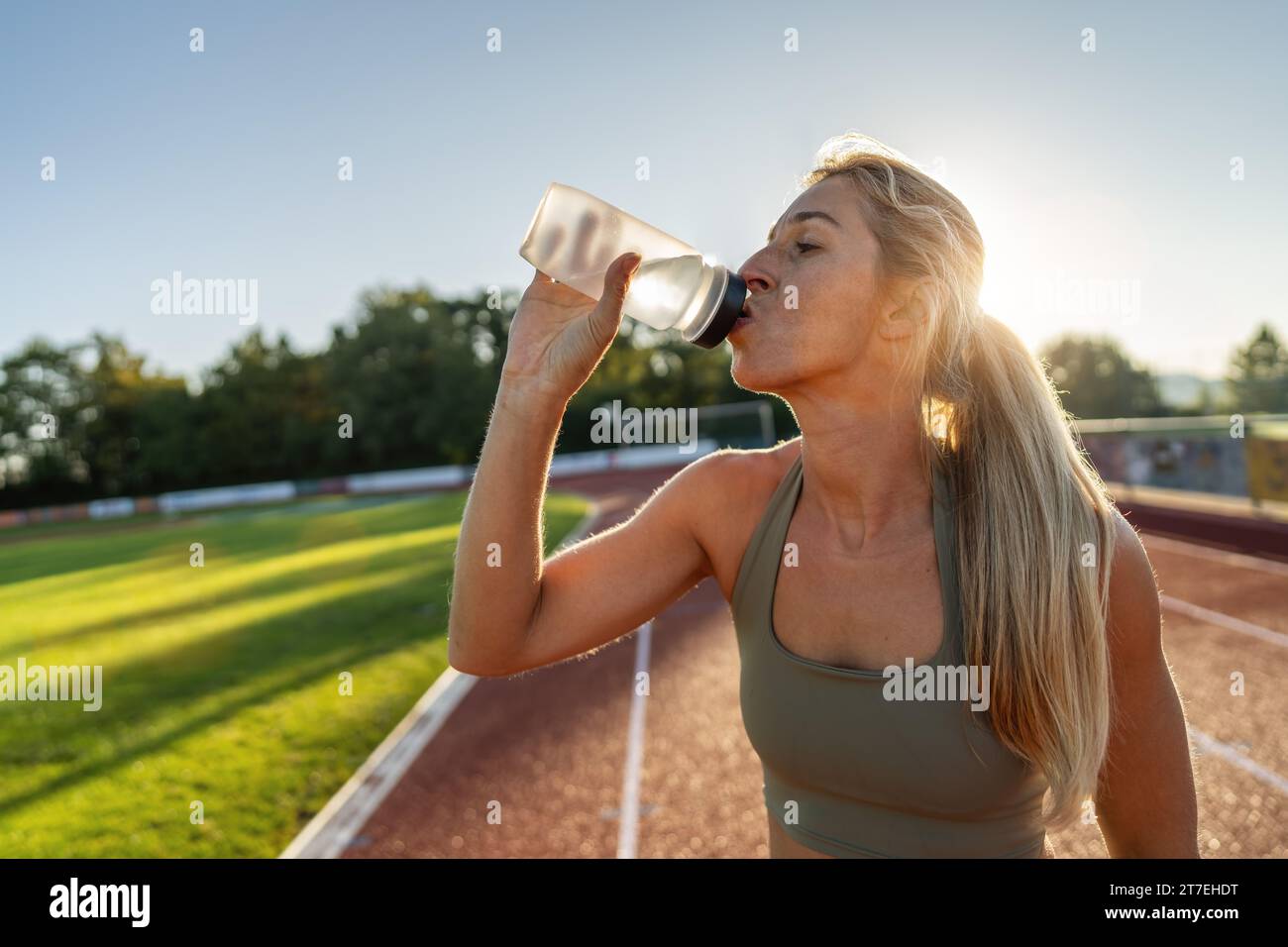 Athletin-Frau trinkt aus einer Wasserflasche auf einem Rennfeld Stockfoto