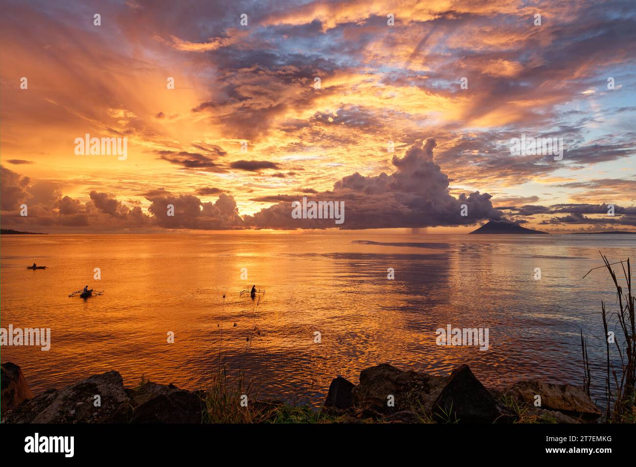 Sonnenuntergang mit spektakulären Farben an der Küste von Sulawesi, die intensiven Farben spiegeln sich im Wasser, drei Fischerboote malerisch im Vorland Stockfoto