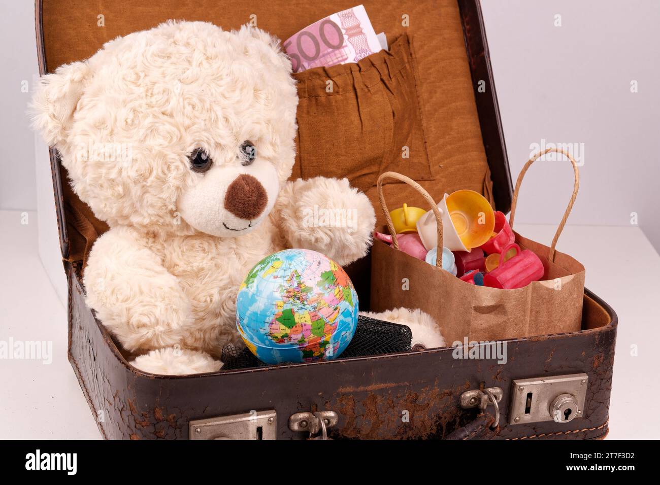 Ein Teddybär sitzt in einem alten Koffer mit einer Kugel. Stockfoto