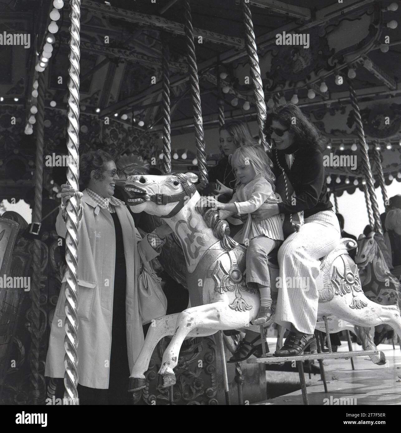 1970er Jahre, historisch, eine Mutter mit ihrer Tochter, die zusammen auf einem Karussell auf einem Jahrmarkt reitet, England, Großbritannien. Die lustige Vergnügungsfahrt ist auch als Karussell bekannt und auch als „Galopper“ bezeichnet. Stockfoto