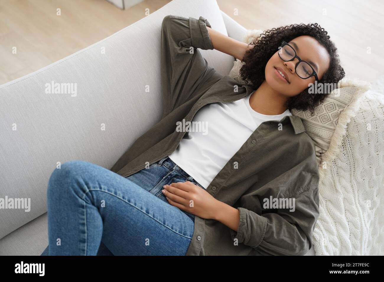 Entspannte schwarze Frau mit Brille auf der Couch, Augen geschlossen, friedlich Stockfoto