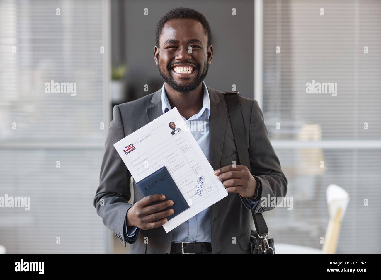 Junger fröhlicher afroamerikanischer männlicher Antragsteller in Formalwear, der in die Kamera schaut, während er ein genehmigtes Visumantragsformular vorzeigt Stockfoto