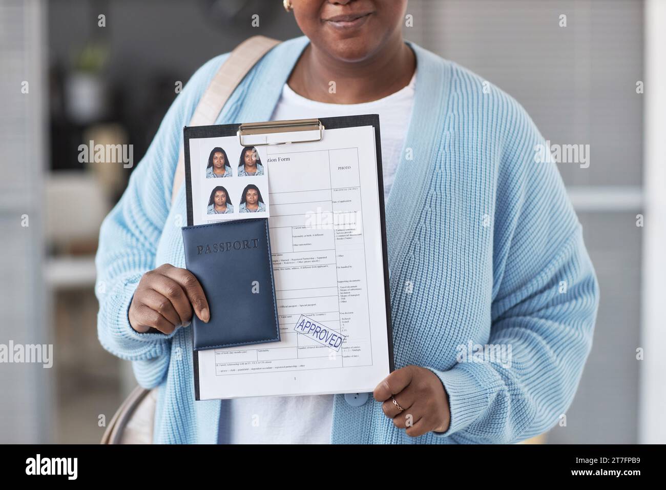 Zugeschnittener Schuss einer jungen afroamerikanischen Frau in blauer Strickjacke mit ausgefülltem Visumantrag mit Genehmigungsstempel Stockfoto