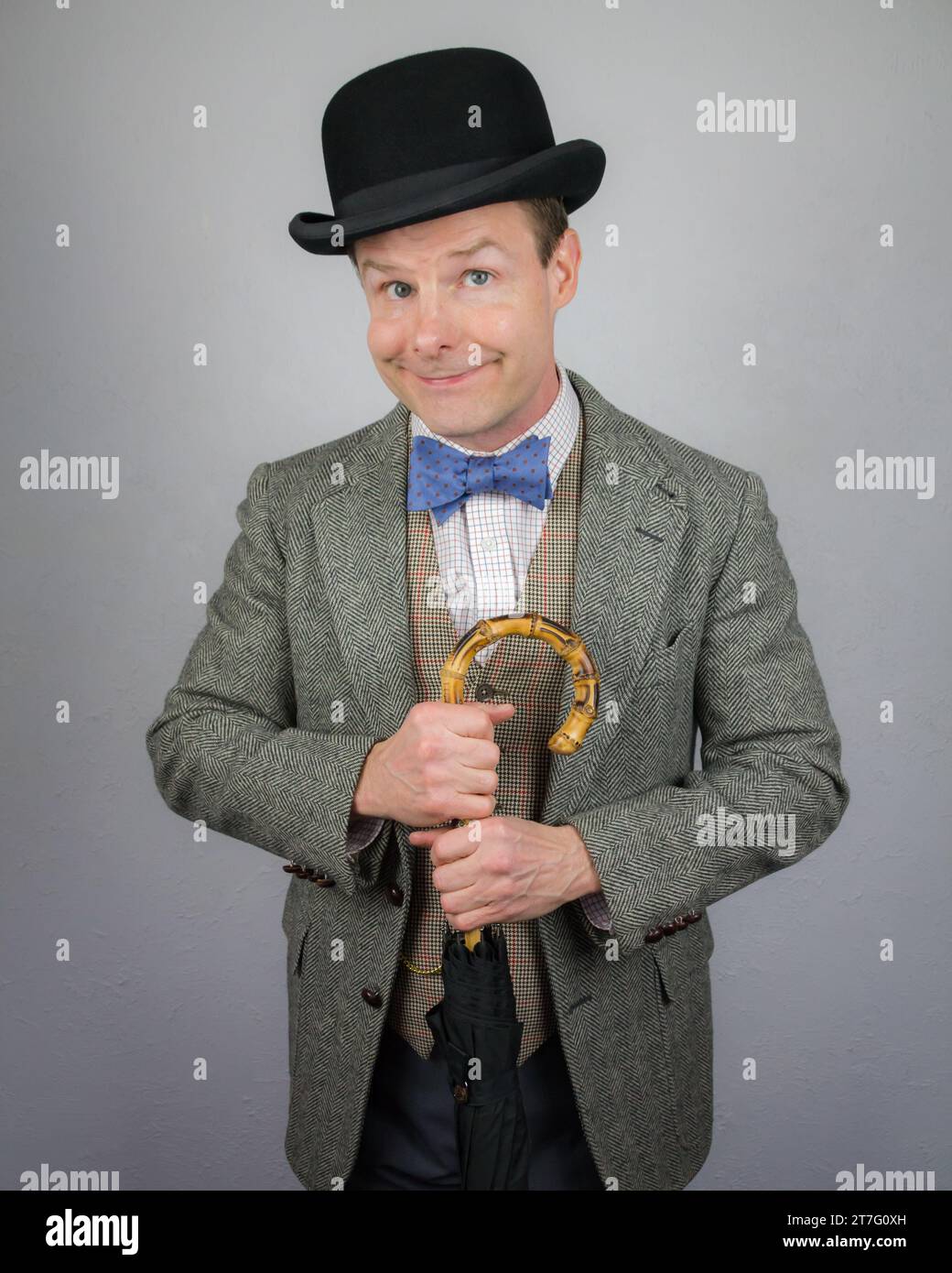 Britischer Charakter im Tweed-Anzug und Bowler-Hut, der einen Regenschirm hält und lächelnd ist. Konzept des Vintage Vaudeville Comic Schauspielers Stockfoto