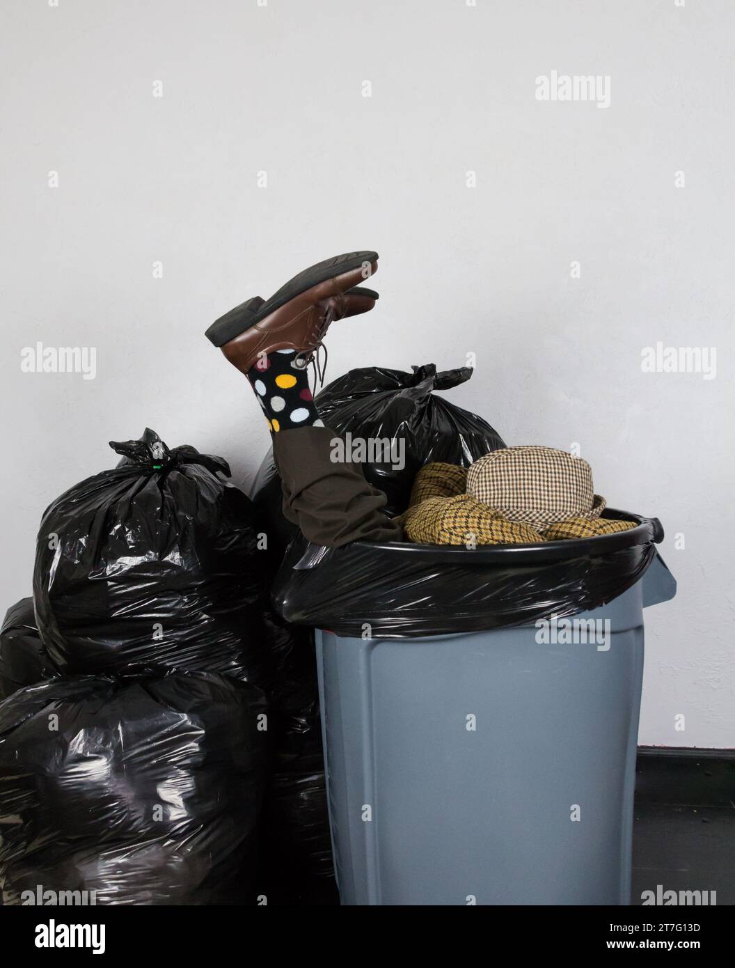 Porträt eines Mannes in Anzug und Hut und Polk-A-Dot Socken, gefüllt in einer Mülltonne, umgeben von Mülltüten. Konzept des Geschäftsmannes weggeworfen. Stockfoto