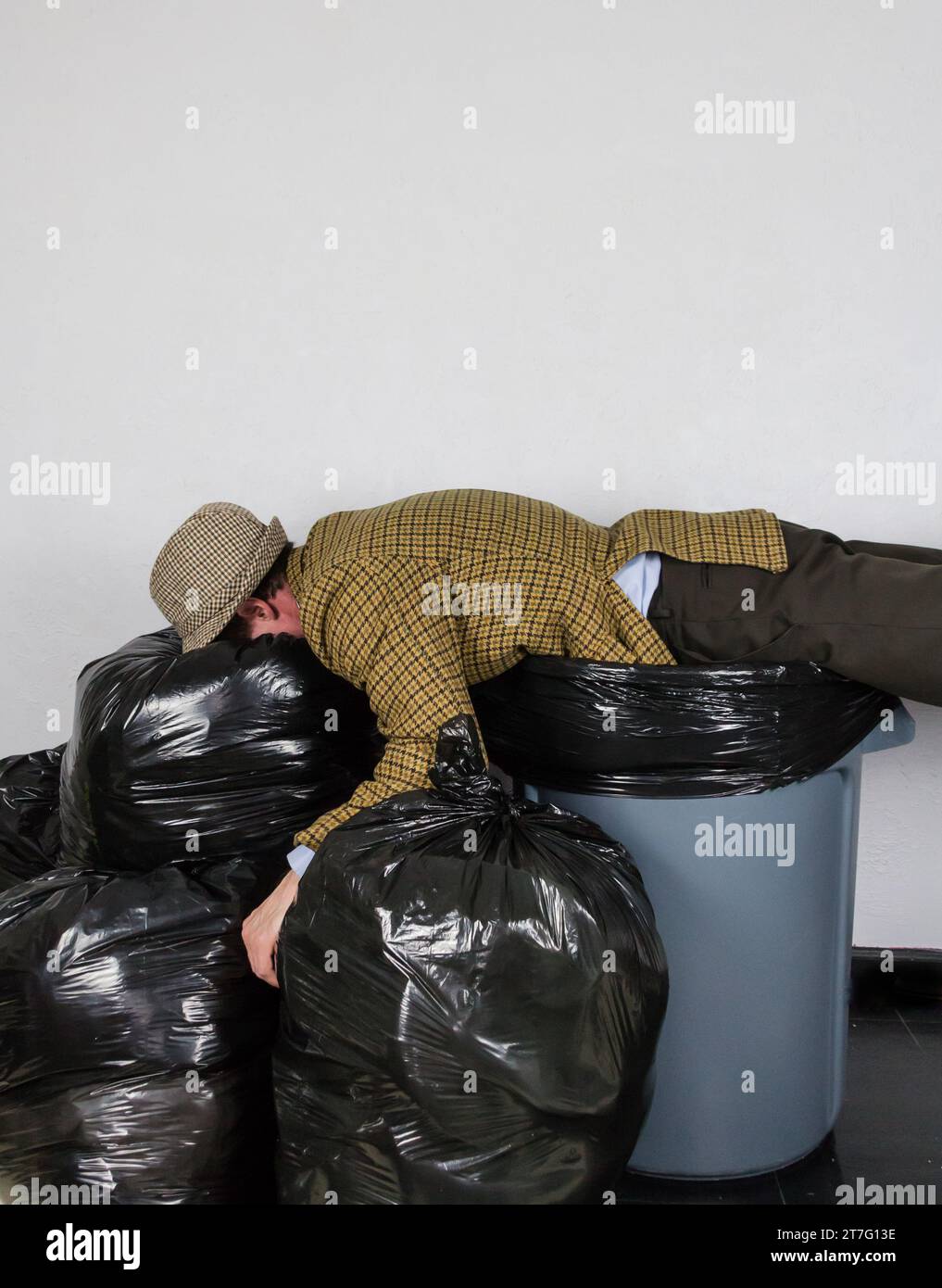 Porträt eines Mannes in hässlichem Anzug, der auf dem Mülleimer liegt und einen Stapel Müllsäcke. Konzept von über einem Zylinder. Mann Weggeworfen. Stockfoto