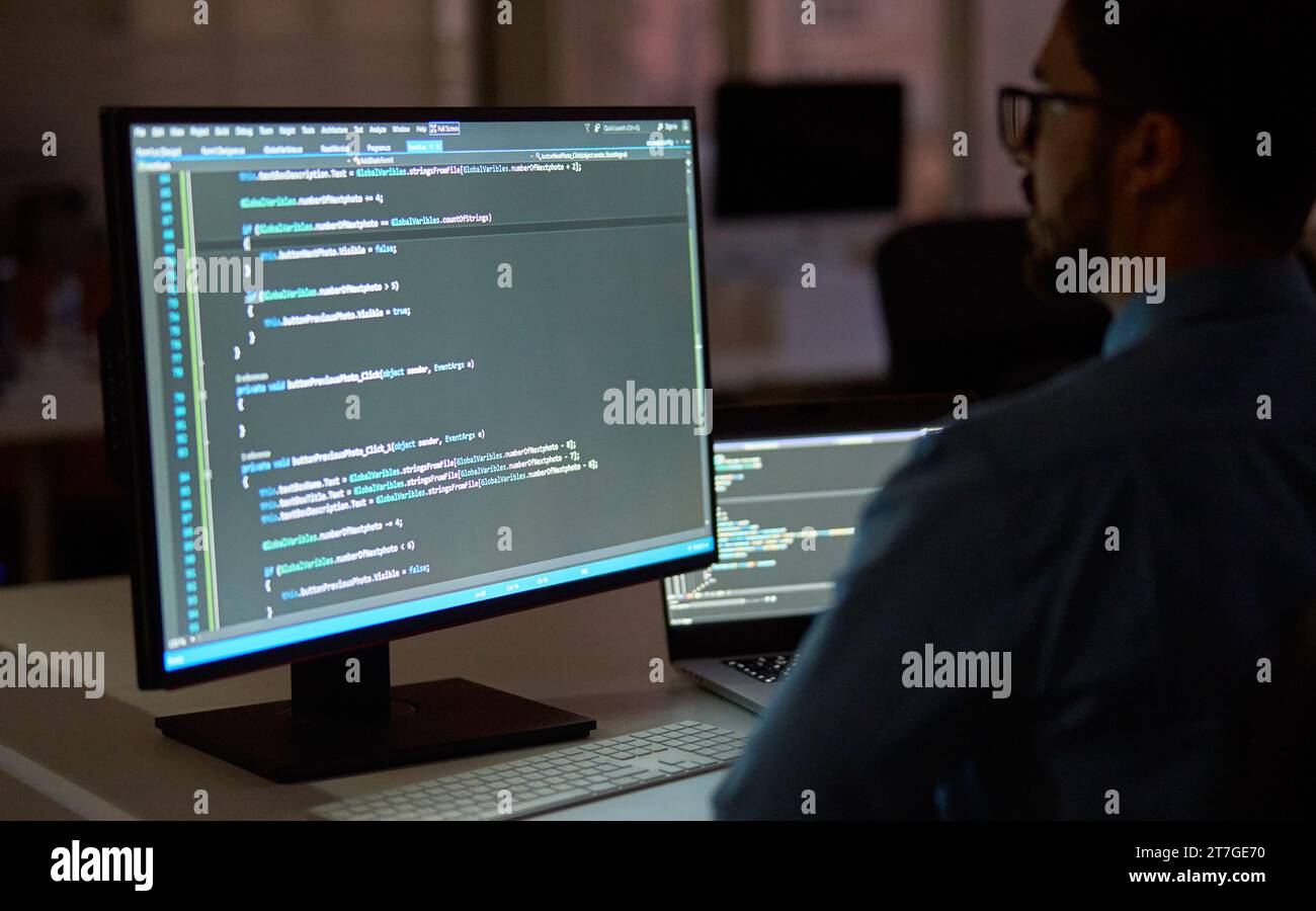 Ein geschäftiger Softwareentwickler, der im dunklen Nachtbüro an einem pc arbeitet. Stockfoto
