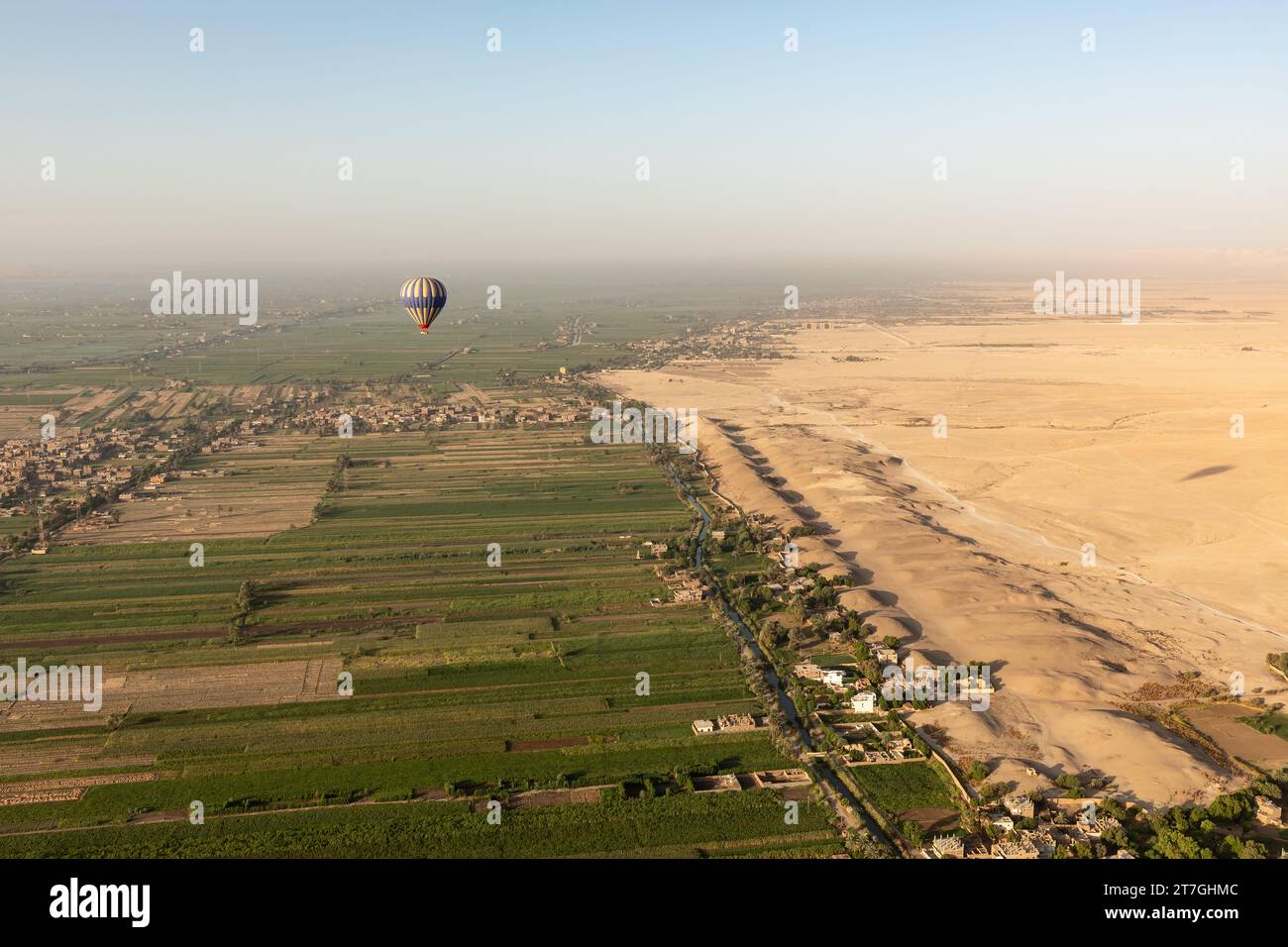 Heißluftballon, der über üppige grüne Felder in der Nähe einer trockenen Wüstenlandschaft schwingt, geht ins Tal der Könige Stockfoto