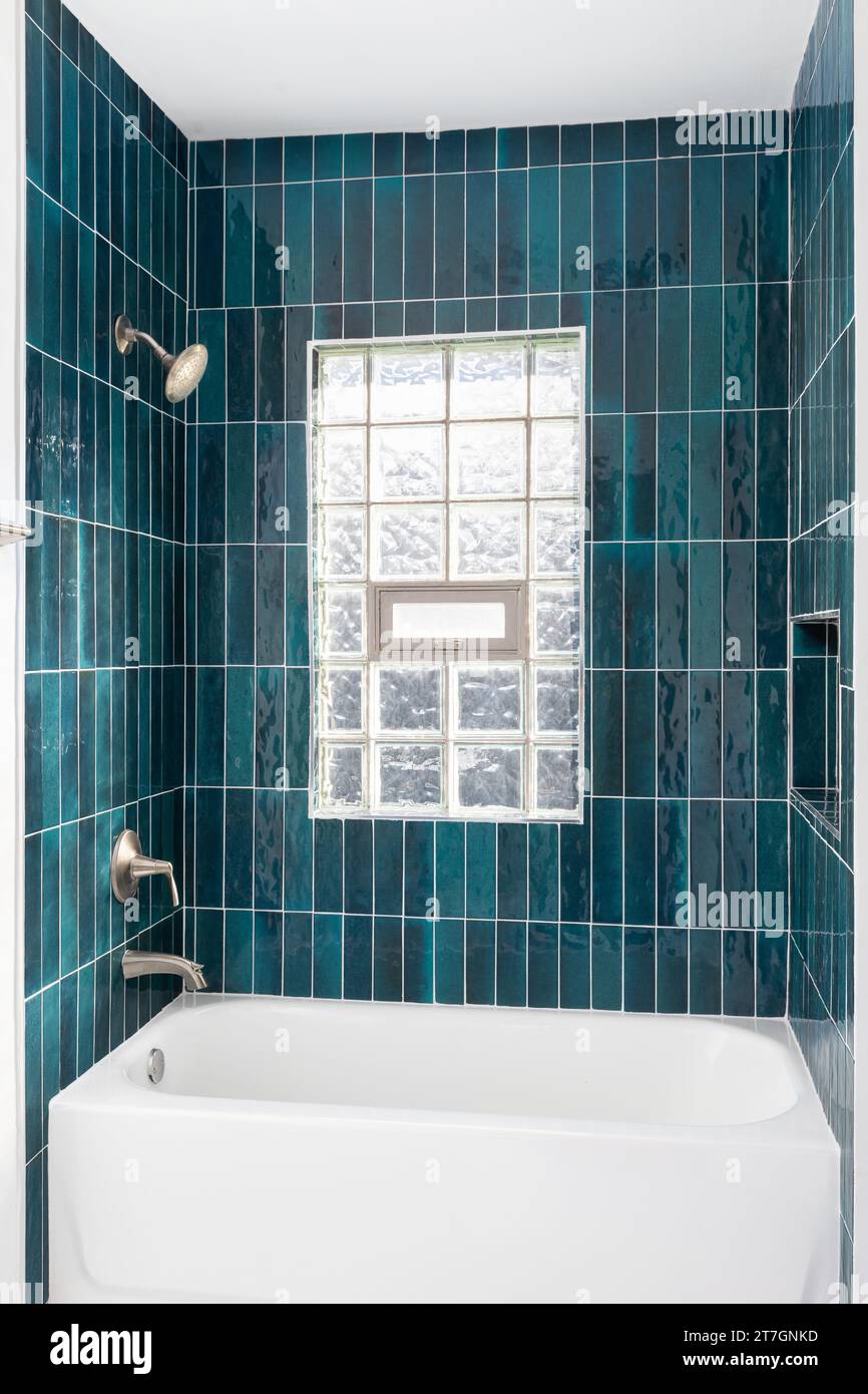 Das Badezimmer verfügt über eine Dusche mit leuchtend blauen vertikalen Glasfliesen, eine eingebaute Nische und ein Fenster mit Glasblöcken. Stockfoto
