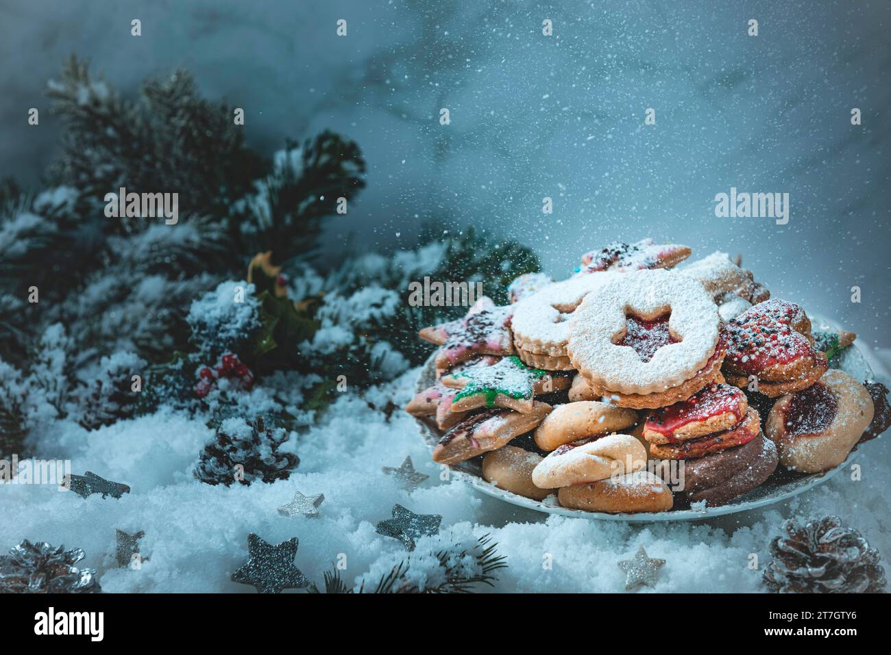 Teller mit verschiedenen Weihnachtskeksen in festlicher Umgebung, Schnee, Tannenzweige, fallender Zucker, künstlerisch Stockfoto