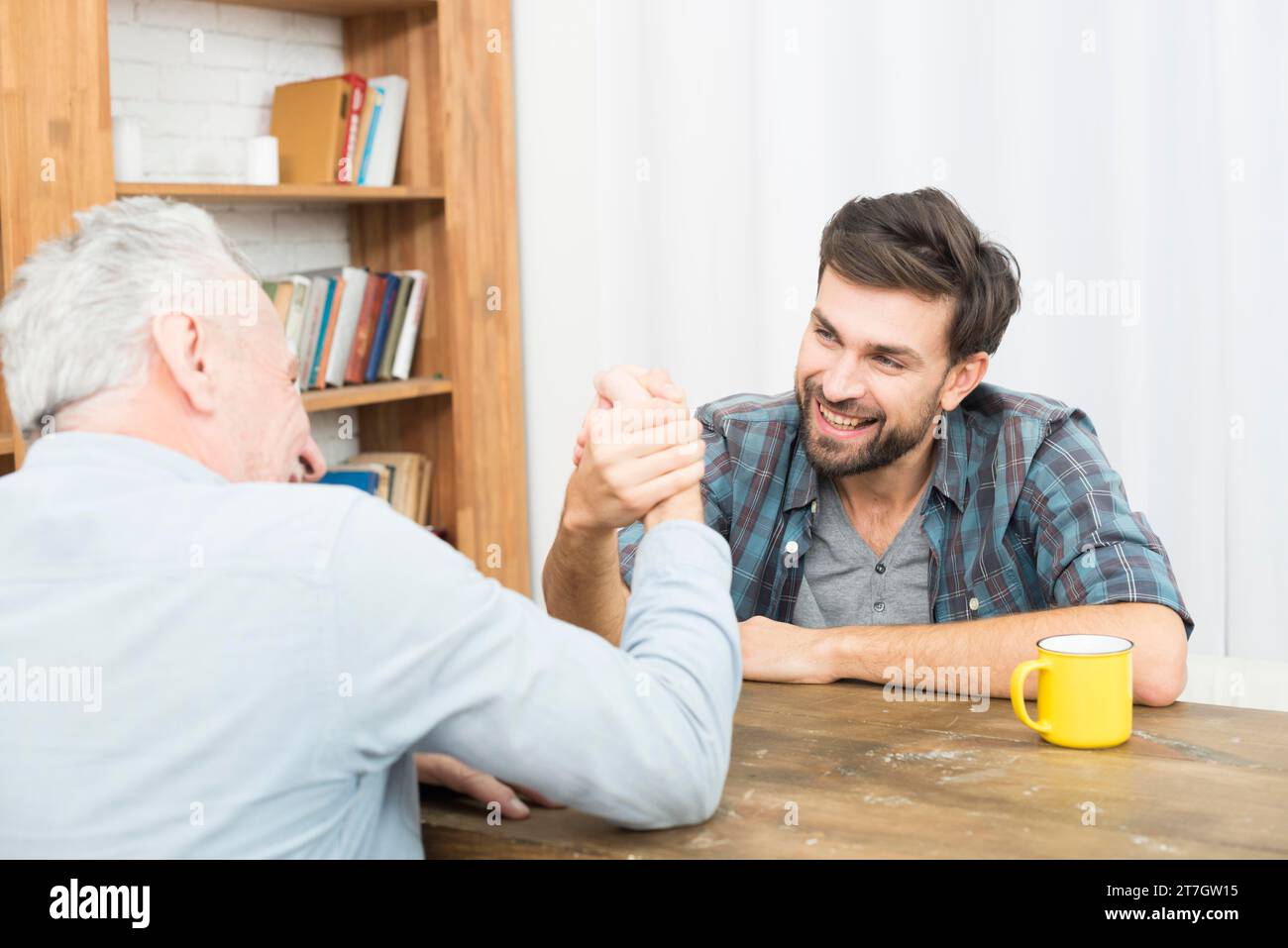 Alter Mann junger glücklicher Kerl mit Händen geklemmt Arm Wrestling Herausforderung Tisch Raum Stockfoto