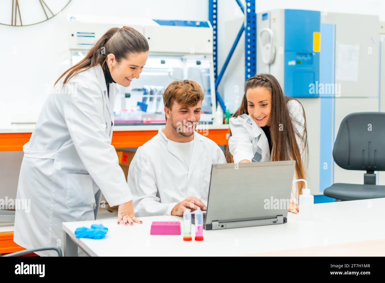 Ein lächelndes und stolzes junges Team von Wissenschaftlern, die in einem Forschungslabor einen Laptop benutzen Stockfoto