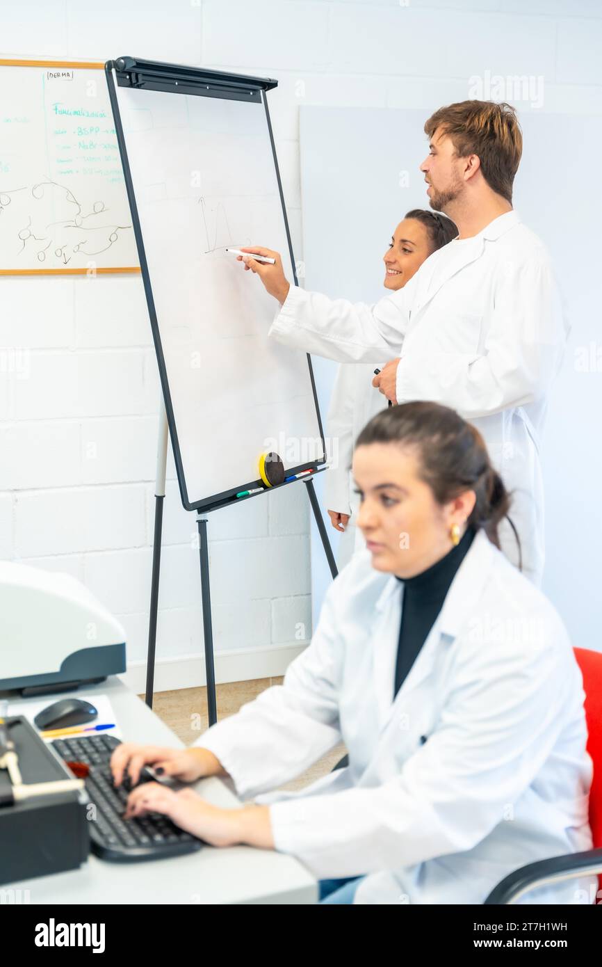 Vertikales Foto eines Wissenschaftlers, der in einem Krebsforschungslabor arbeitet, mit Computer und Schrift auf einem Whiteboard Stockfoto