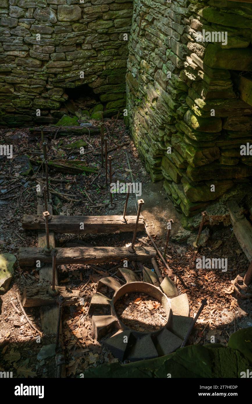 Ansicht einer schattigen steinernen Ruine mit Laub bedeckt, einem verrosteten Metallrahmen und einem radähnlichen Eisenteil in der Sonne, Robert H. Treman State Park, New York. Stockfoto
