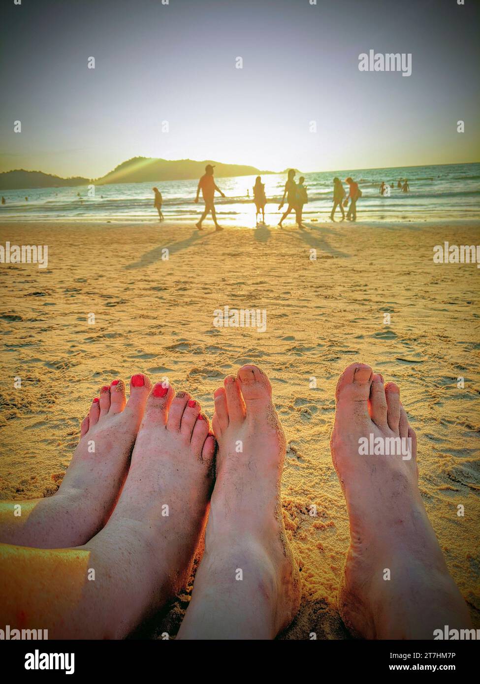 Ein paar Rast am Patong Beach in Phuket, Thailand bei Sonnenuntergang mit nur den Füßen zu sehen, die Menschen und das Meer im Hintergrund unscharf. Stockfoto