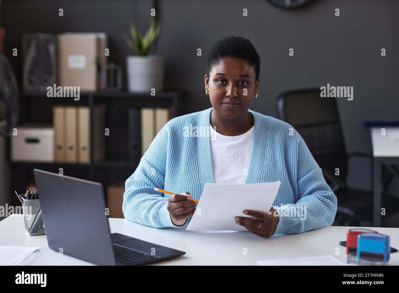 Junge, selbstbewusste Managerin des Visa-Antragszentrums in Casualwear, die auf die Kamera blickt, während sie am Arbeitsplatz sitzt und Daten überprüft Stockfoto