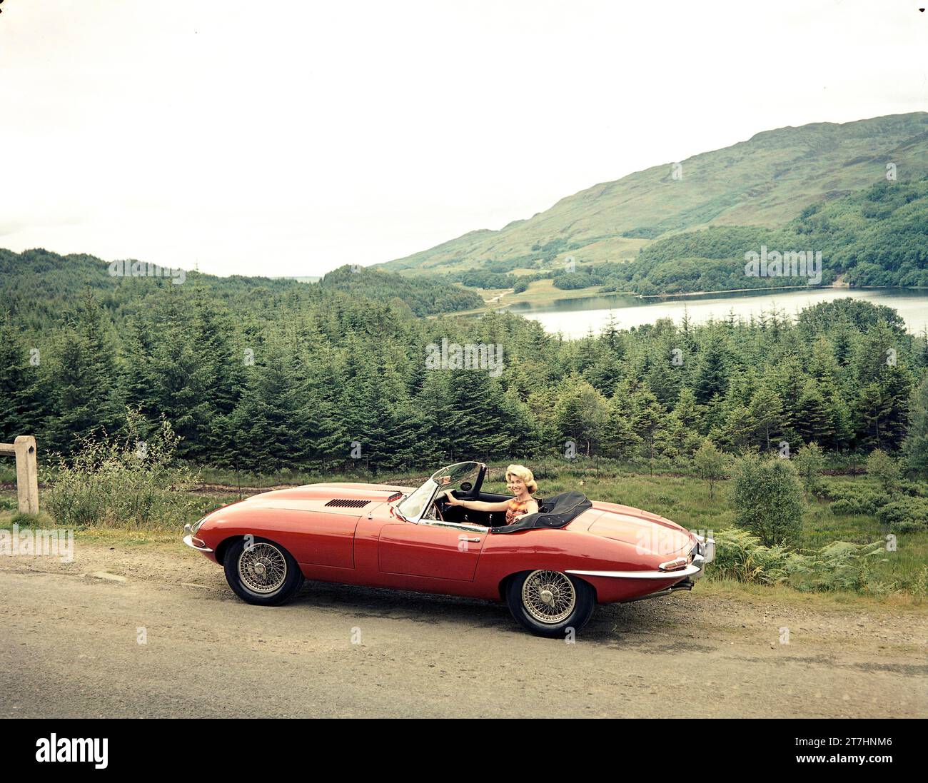 1961 Jaguar E-TYPE Roadster der Serie 1 in schottischen Highlands mit weiblichem Modell im Fahrersitz Stockfoto