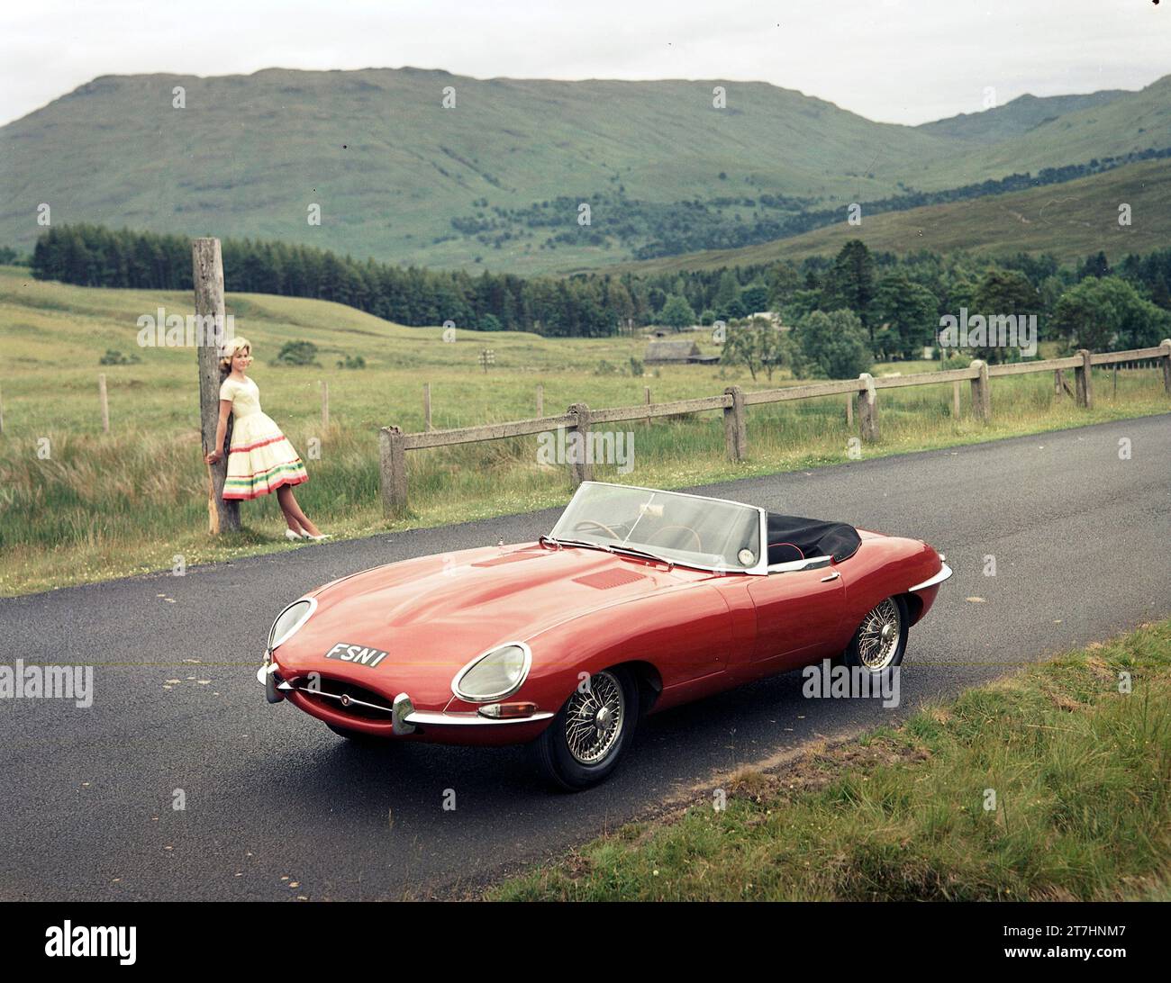 1961 Jaguar E-TYPE Serie 1 Roadster in schottischen Highlands mit weiblichem Modell, das an einen Holzpfosten gelehnt ist Stockfoto