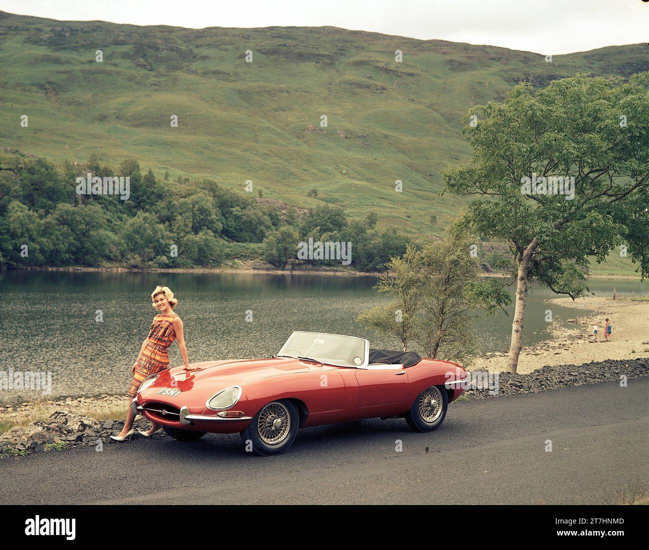 1961 Jaguar E-TYPE Roadster der Serie 1 neben einem Loch in den schottischen Highlands mit weiblichem Modell auf der Motorhaube Stockfoto