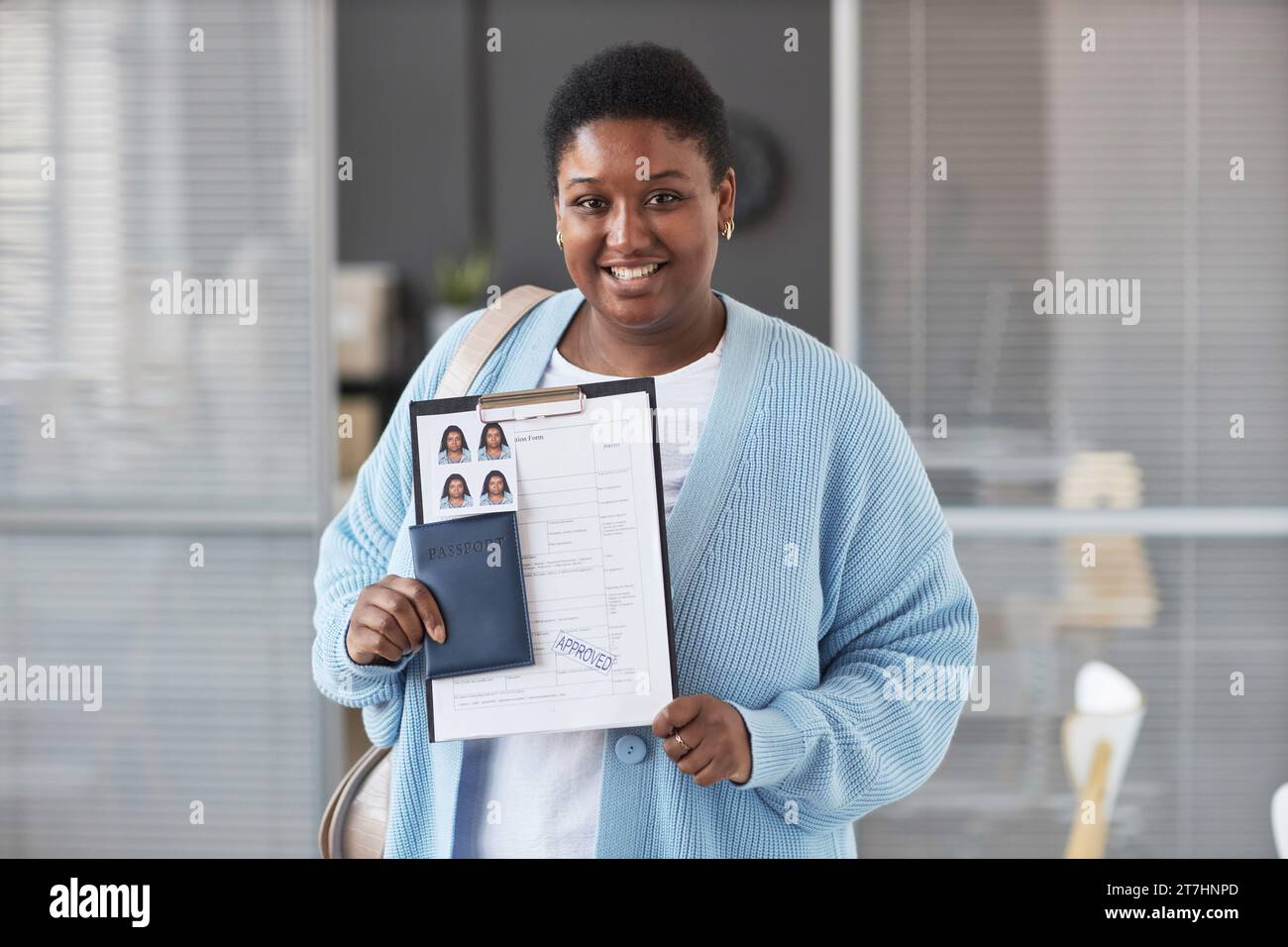 Junge afroamerikanische Bewerberin in Casualwear, die mit einem Lächeln in die Kamera schaut, während sie ein genehmigtes Visumantragsformular vorzeigt Stockfoto