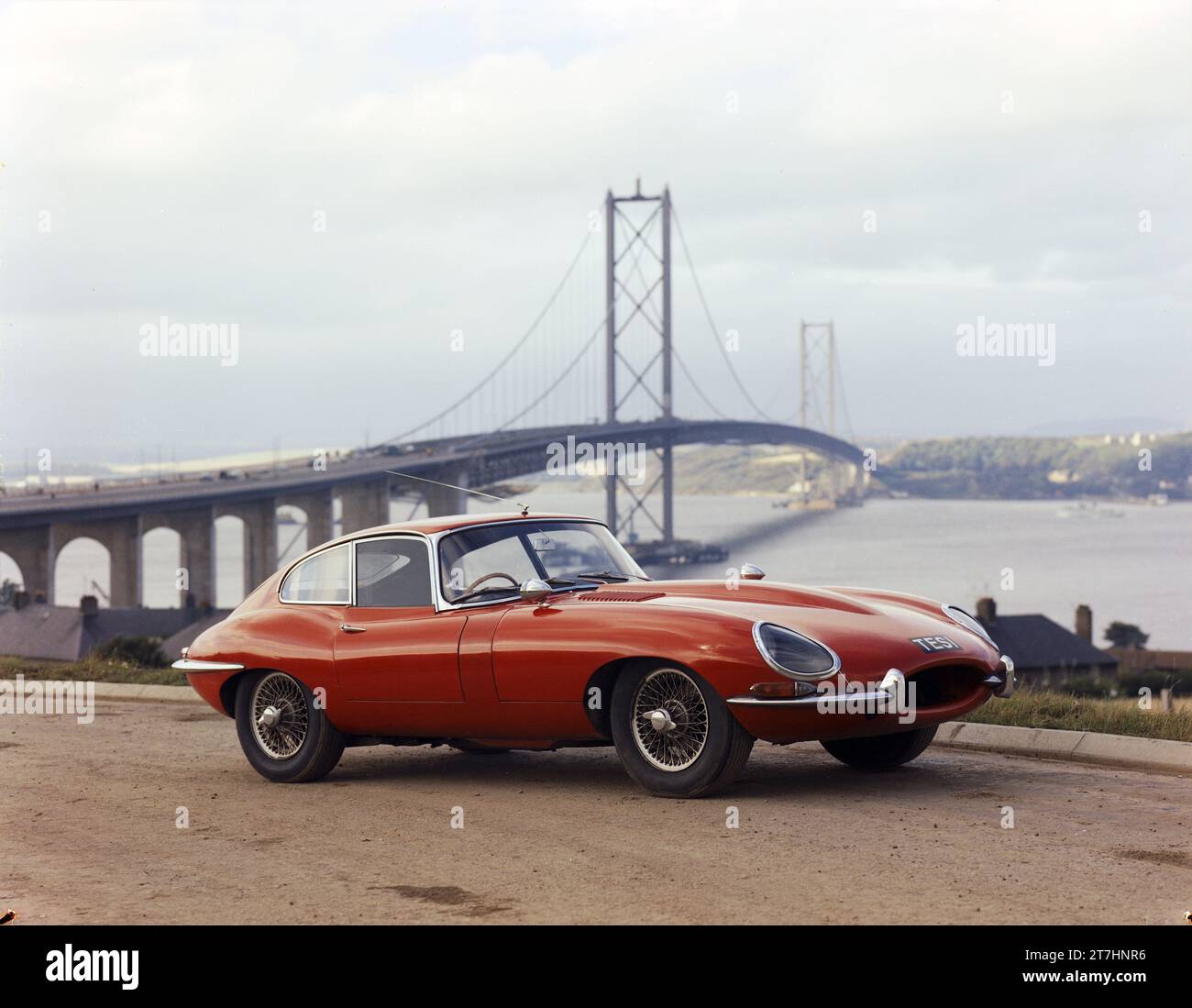 1964 Pressebild des roten Jaguar E-TYPE Serie 1 Coupé, TES 1, mit der neu eröffneten Forth Road Bridge im Hintergrund Stockfoto