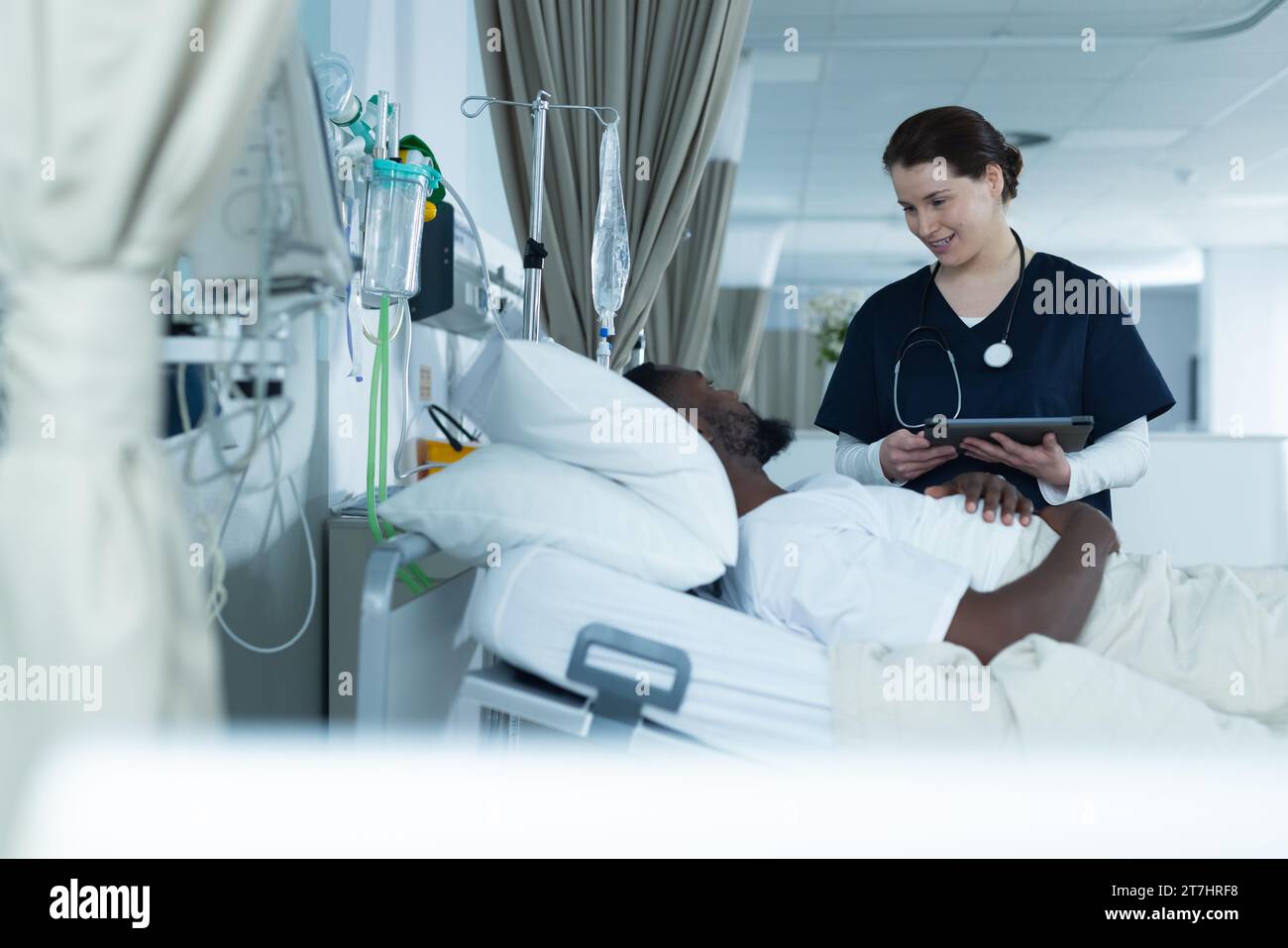 Diverse Ärztin und männliche Patientin liegt im Bett und spricht im Krankenhauszimmer Stockfoto