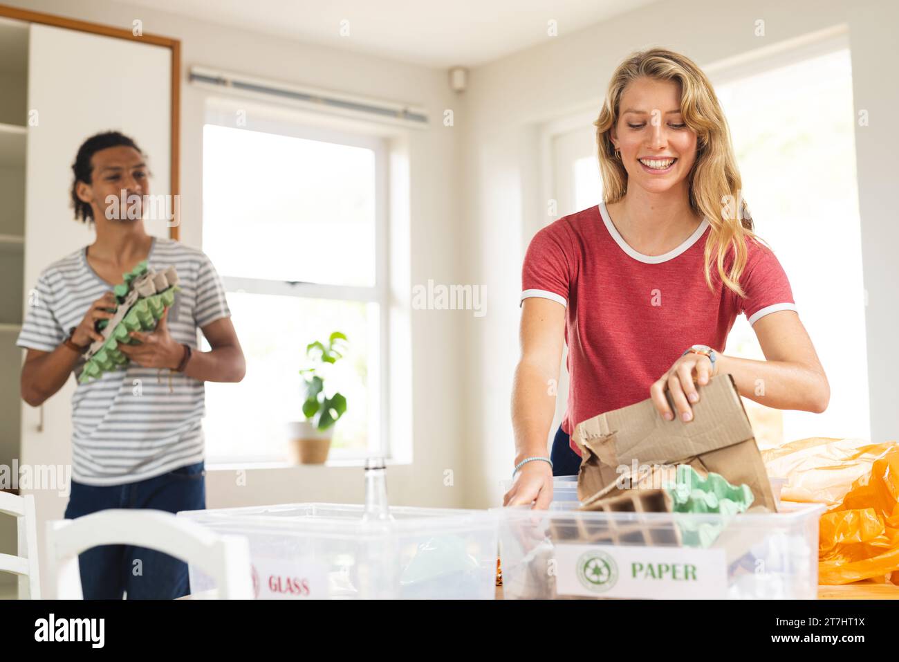 Glückliche, vielfältige Paare sortieren Müll zum Recycling in der sonnigen Küche zu Hause Stockfoto