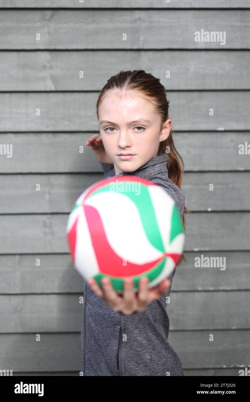 Teenager-Mädchen, das Volleyball in der linken Hand hält, bereit, mit direktem Augenkontakt zu dienen Stockfoto