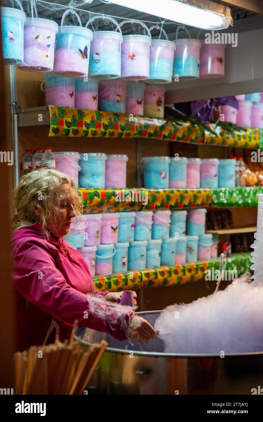 Zuckerträume wurden in die Realität umgesetzt: Eine geschickte Frau versprüht Magie an einem Straßenstand und kreiert den süßen Charme von Zuckerwatte im städtischen Glanz. Stockfoto