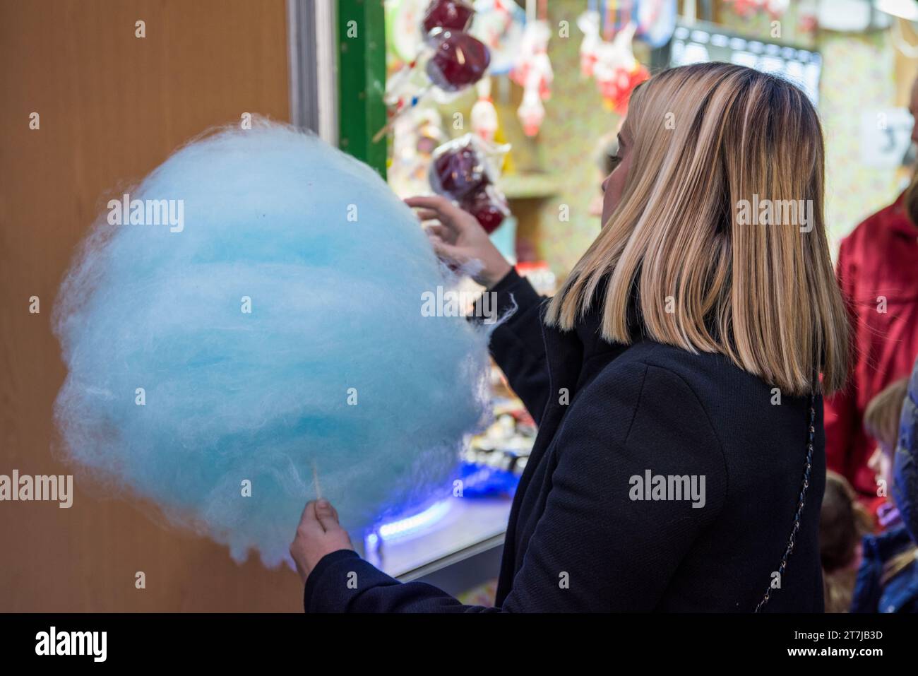 Im Weihnachtsgeist: Eine Frau genießt auf der Weihnachtsmesse Barcelonas fröhlich eine leuchtende blaue Zuckerwatte und verleiht dem fe einen Hauch süßer Magie Stockfoto