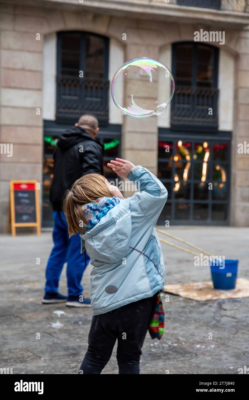 Gothic Quarter Joy: Die Freude eines Kindes, wenn es mit übergroßen Seifenblasen spielt und die historischen Straßen Barcelonas winterliche Wunder bereithält Stockfoto