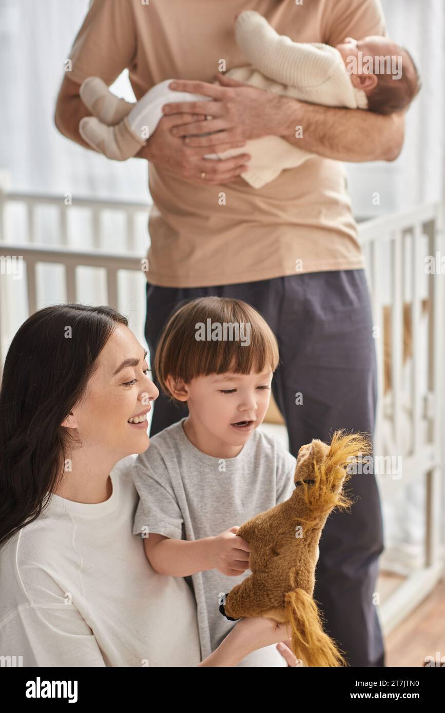 Vertikale Aufnahme einer fröhlichen Mutter, die mit ihrem kleinen Sohn spielt, mit Spielzeugpferd, Familienkonzept Stockfoto