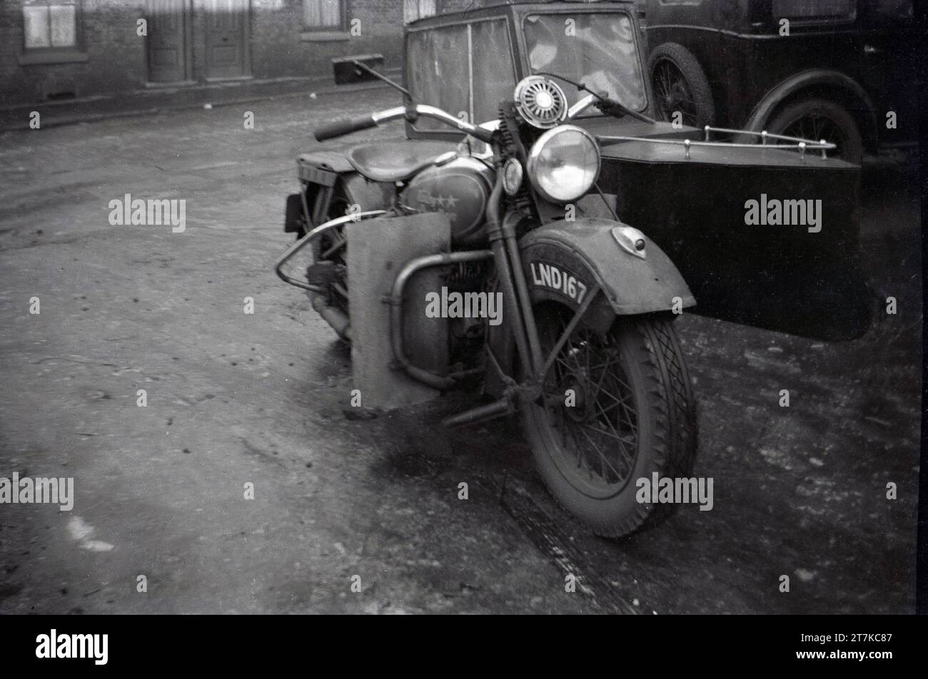 1950er Jahre, ein amerikanischer Harley Davidson Motorrad und Beiwagen, der in einer Seitenstraße in Oldham, England, Großbritannien, geparkt wurde. Das Motorrad ist möglicherweise ein WL, ein Modell aus der Zeit vor dem Zweiten Weltkrieg. Das Design des Beiwagens ist interessant und sieht aus wie ein kleines Boot mit geschlossenem Dach. Stockfoto