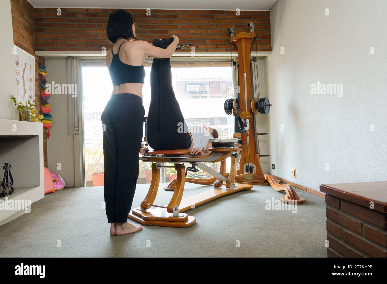 Zwei nicht erkennbare Weibinnen, die körperliches Training mit Pulley-Maschine und Gewichten zu Hause machen, Beine und Bauch trainieren. Stockfoto