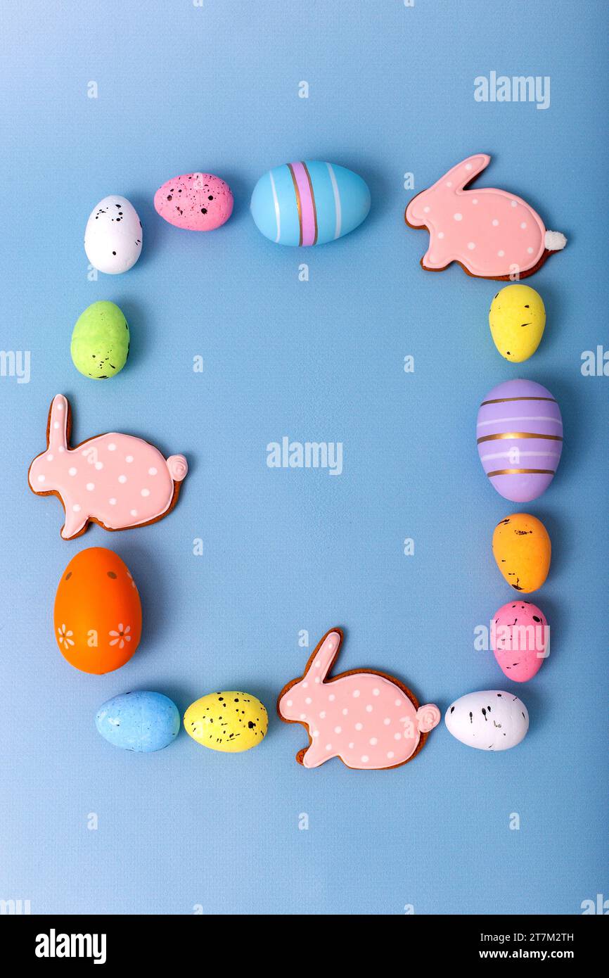 Rechteckiger Rahmen von mehrfarbigen Ostereiern und Lebkuchen in Form von rosa Kaninchen Stockfoto
