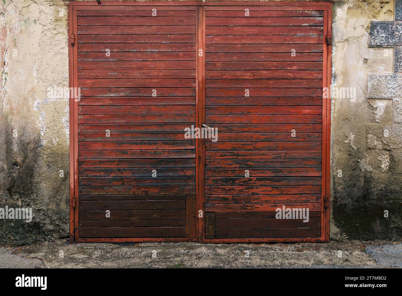 Rote Doppeltüren aus Holz und abgenutzte Zementwand eines antiken Gebäudes. Stockfoto