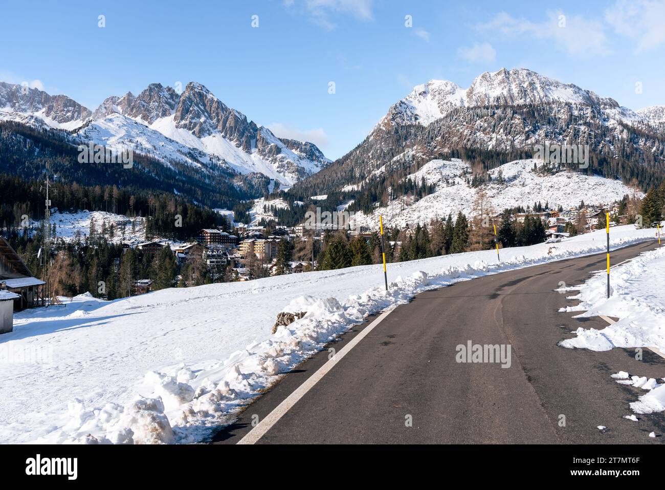 Straße, die zu einem Bergdorf führt, umgeben von majestätischen Bergen, die im Winter mit Schnee bedeckt sind Stockfoto