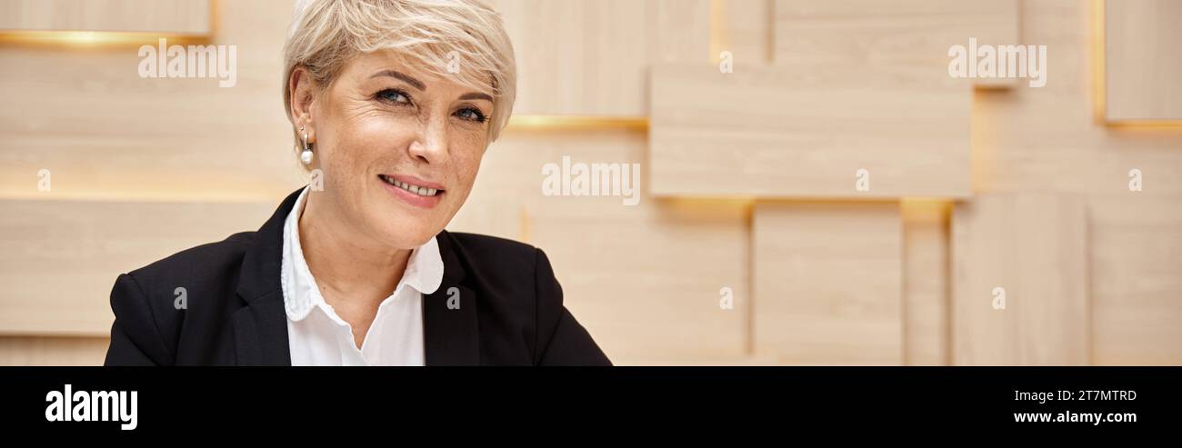 Glücklicher Immobilienmakler mittleren Alters mit kurzen Haaren, die in einem Immobilienbüro arbeiten, arbeitsreiche Banner Stockfoto